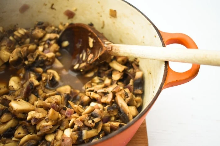 A casserole pot with cooked mushrooms and a wooden spoon