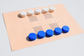 na zdjęciu plansza do gry w Tandemy oraz początkowe ustawienie pionów, w dolnym rzędzie pięć niebieskich pionów a w górnym pięć białych