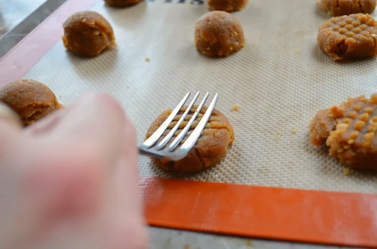 A fork making a crisscross pattern one peanut butter cookie dough balls on a silpat lined baking sheet.