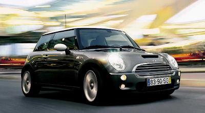 Photo of a new, sleek, grey Mini Cooper on the road with a sunset in the background