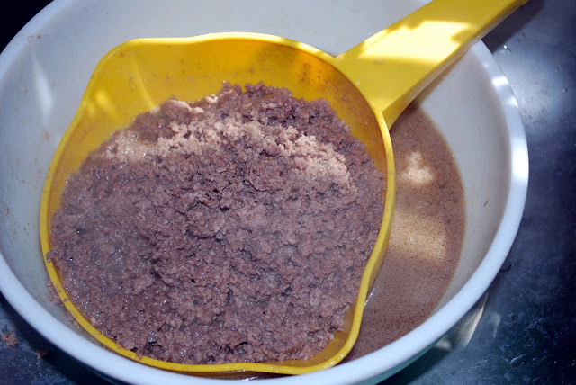 A yellow plastic strainer set inside a large white bowl. The strainer holds the cooked ground beef, the cooking water is caught by the bowl.