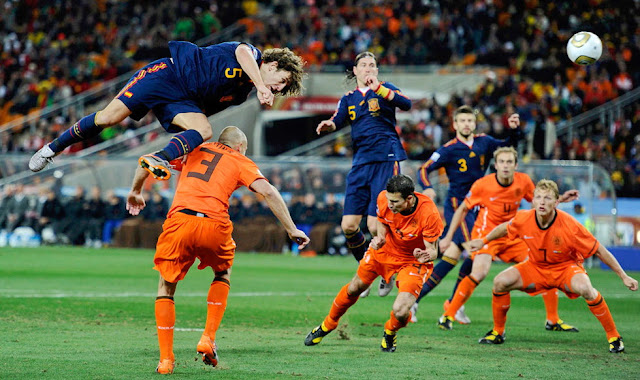 Carles Puyol remata de forma espectacular imponiéndose a Heitinga en el salto. Sergio Ramos, Van Persie, Piqué, Mathijsen y Kuyt permanecen atentos a la jugada. SELECCIÓN DE ESPAÑA 1 SELECCIÓN DE PAÍSES BAJOS 0 Domingo 11/07/2010, 20:30 horas. XIX Copa Mundial de Fútbol Sudáfrica 2010, Final. Johannesburgo, Sudáfrica, estadio Soccer City: 84.490 espectadores. GOLES: 1-0: 116’, Iniesta. ESPAÑA GANA EL CAMPEONATO MUNDIAL DE FÚTBOL.