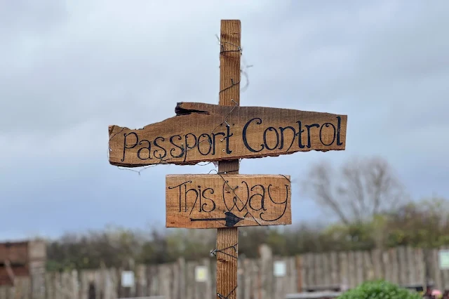 a rustic wooden sign with writing on saying "passport control this way"