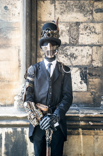 Steampunk man wearing black spandex skin suit/bodysuit costume with a 3 piece suit, top hat, goggles, gauntlets, bracers, mask and cane. mens steampunk costumes