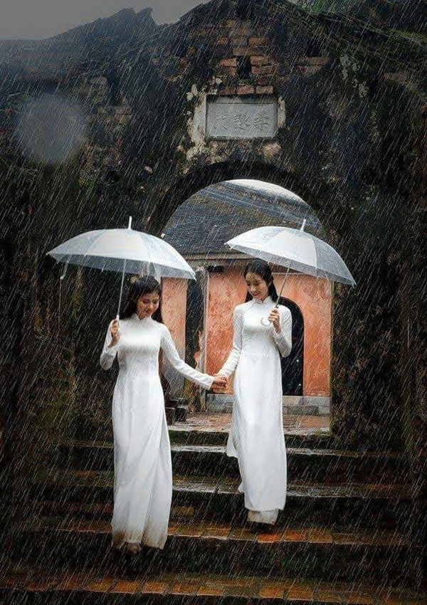 Hai thiếu nữ áo dài trắng che dù trong mưa