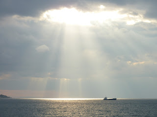 Sun shining through clouds onto a big boat in the ocean near the Akashi Kaikyo Bridge, Maiko, Kobe