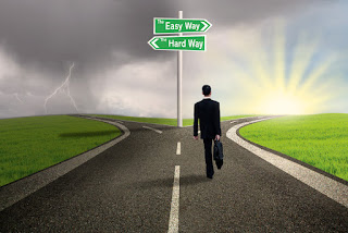 A business man walks along a street to a fork with 2 choices: the easy or the hard way
