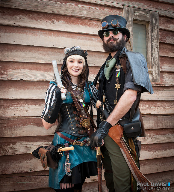 Steampunk couple (man and woman) at wild wild west con wearing blue pleather dress, aviator helmet, goggles, etc.