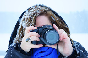 Mulher com capus, tirando foto na neve. Os cabelos cheios de neve como caspa.