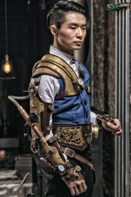 Steampunk man wearing blue waistcoat (vest), trousers, leather armor, leather steam arm. Men's steampunk fashion and costumes