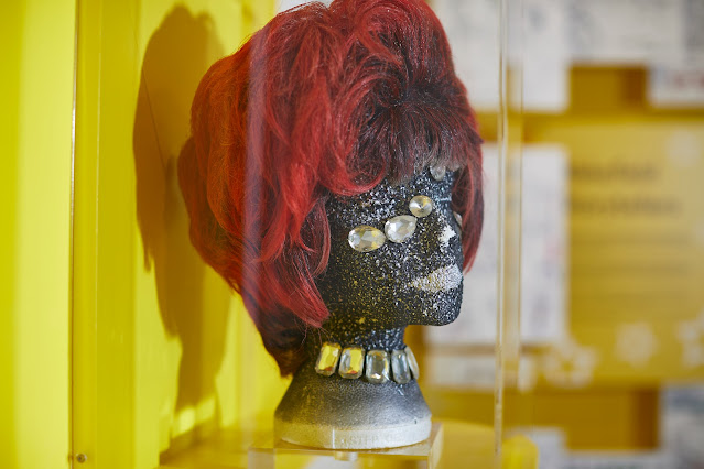 A bright red bobbed wig with darker red undertones, on a bejewelled and glittery mannequin head on display at Wakefield Museum