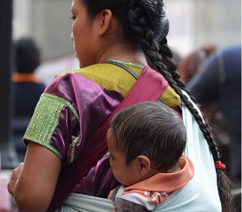 Image: Young street vendor with baby carried in a rebozo in the main square of the city of Oaxaca, Mexico, by Alejandro Linares Garcia on Wikipedia