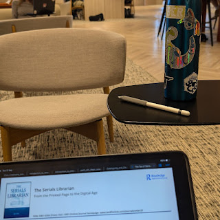 Computer screen that reads the Serials librarian, a chair a table and a bottle with stickers on it