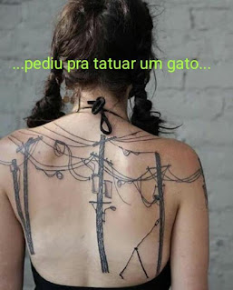 Foto. Uma pessoa de costas, cabelos castanhos escuros repartidos e presos em duas tranças, uma de cada lado. Ela usa uma frente única preta. A tatuagem preta se destaca na pele clara das costas, de ombro a ombro: vários postes de luz com uma gambiarra de fios emaranhados e extensões soltas. Frase sobreposta acima da nuca em letras verdes: ...pediu pra tatuar um gato...