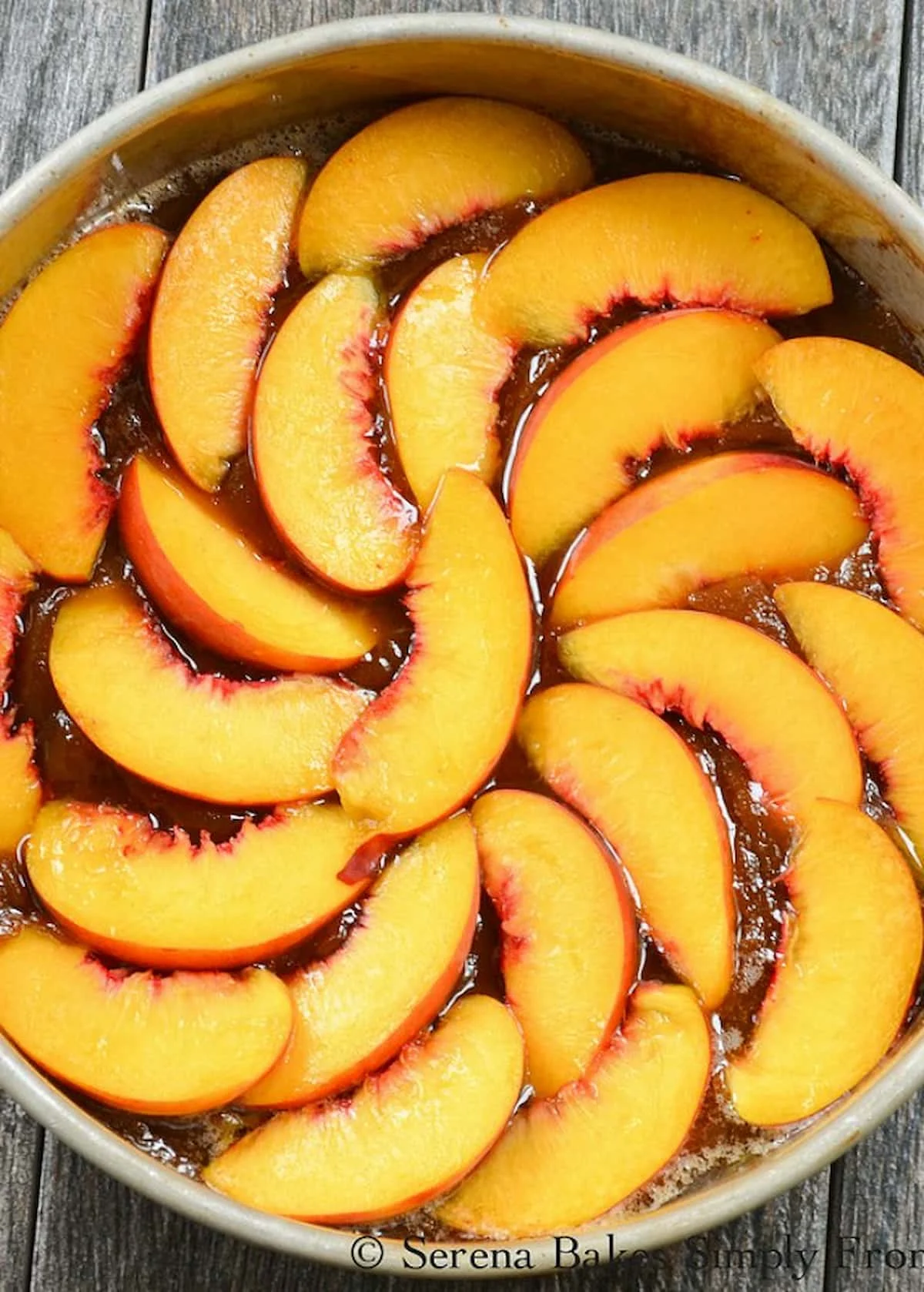 A cake pan filled with the caramelized sugar and butter mixture then topped with sliced peaches going in a circle.