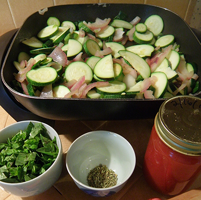 Frying pan with onions and Zucchini, herbs and tomato juice in foreground