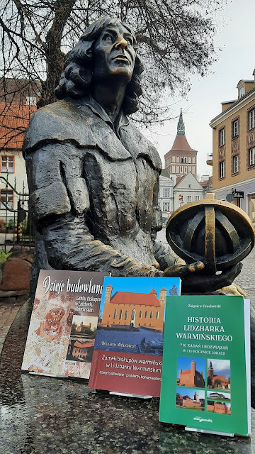 trzy książki opisująe Lidzbark Warmiński na tle pomnika Kopernika
