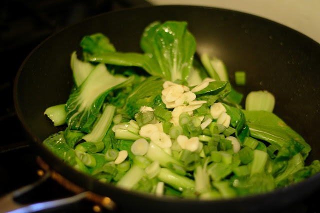 The green onions and garlic being added to the bok choy in a frying pan. 