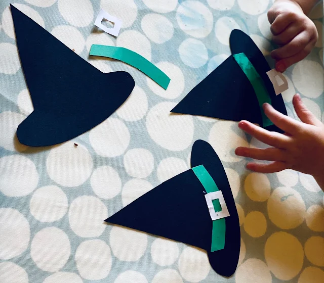 A 3 year old gluing on a white buckle onto a cardboard witches hat