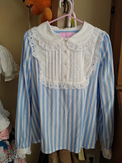 A blue and white stripped blouse with a white yolk that has eyelet lace and a Peter Pan collar. The cuffs also have eyelet lace as well.