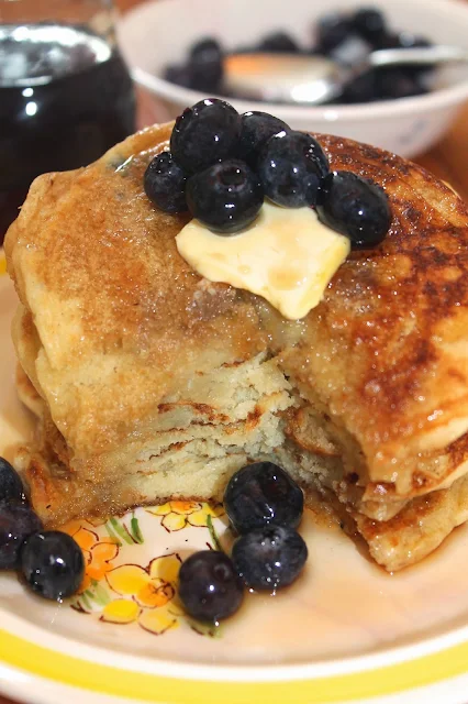 Stack of sourdough pancakes topped with blueberries, butter, and maple syrup.