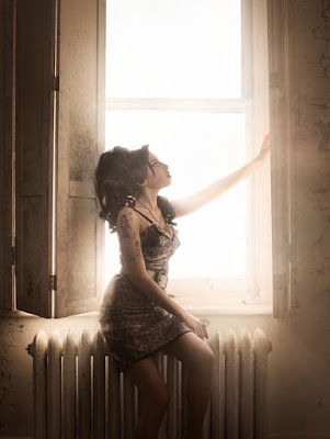 Amy Winehouse sitting in a window with light surrounding her 