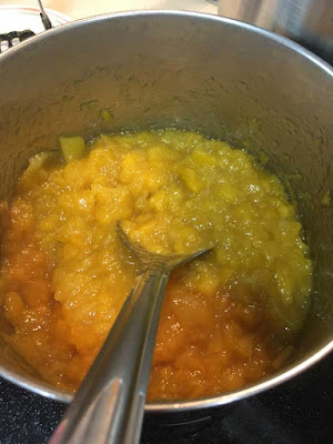 A silver pot with a deep layer of thick, cooked-down mango chunks at the bottom, with a flat silver spoon resting in the mango.