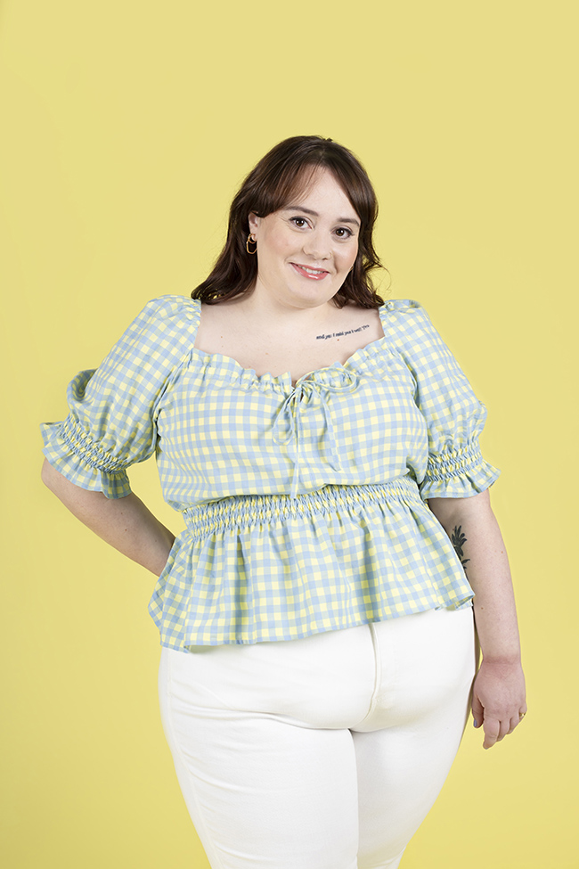 Plus size brunette woman wearing a blue and yellow gingham Mabel blouse with shirring at waist and on sleeves