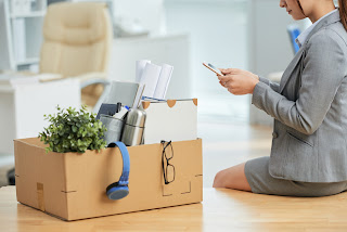 Woman sitting on desk with packed box of belongings