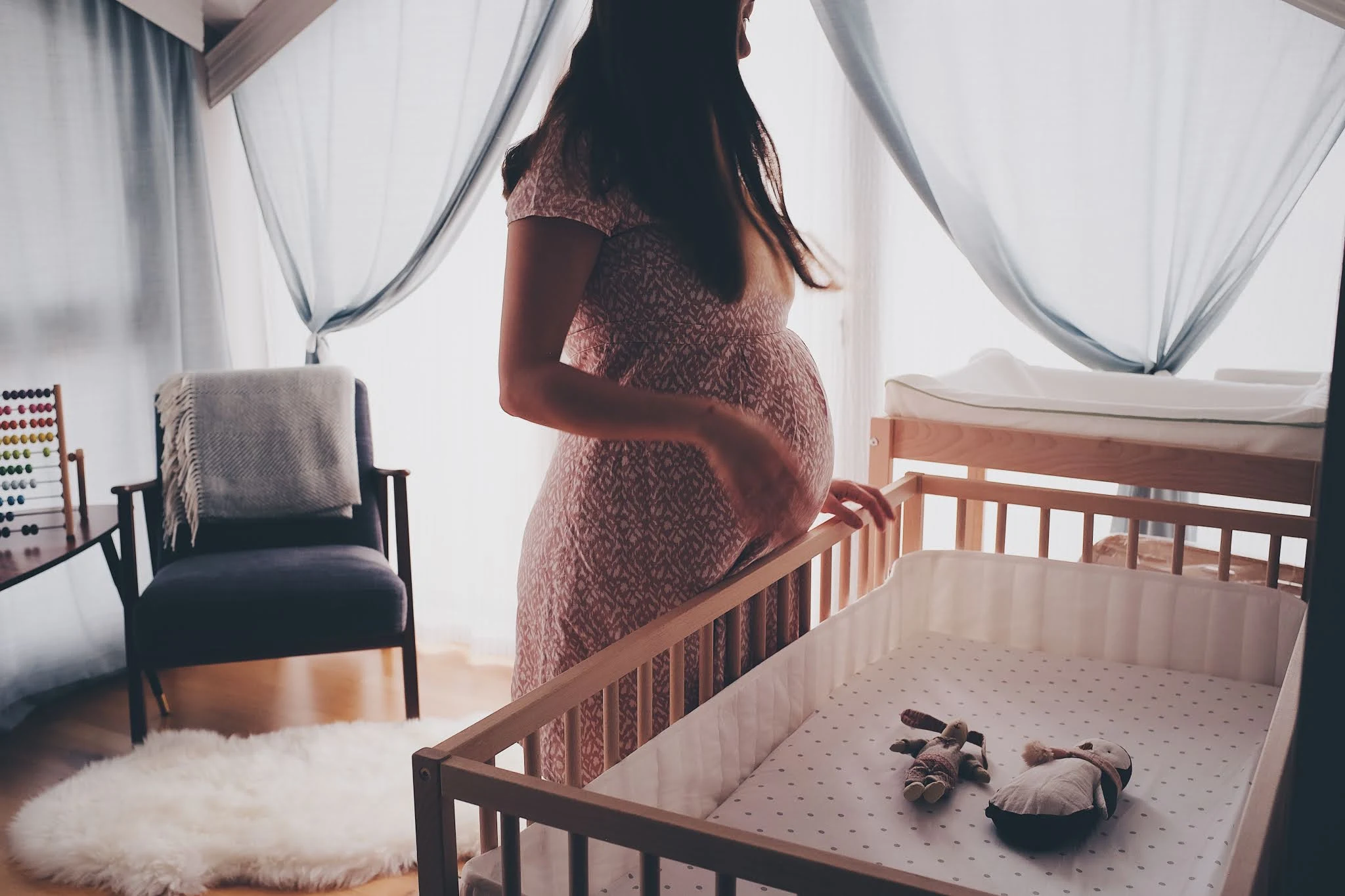 A pregnant woman in a nursery looking into a cot, royalty free image from Unsplash