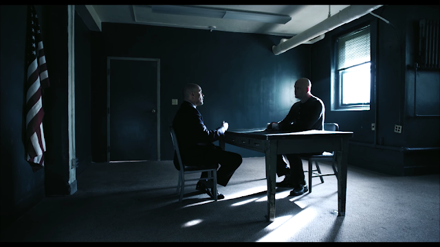 Two men talk in a room while the American flag watches closely for its chance to escape.