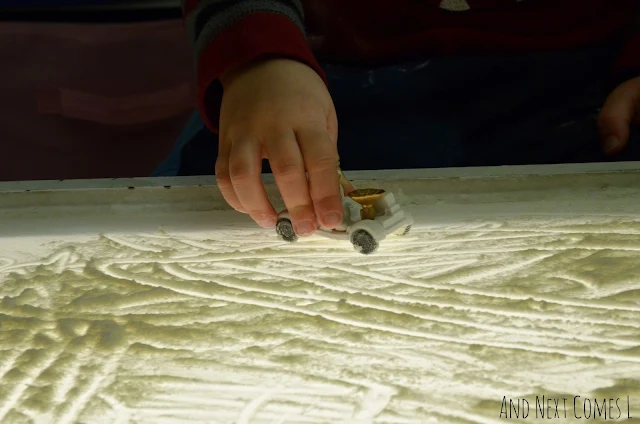 Closeup of toddler's hand driving a moon rover figurine through moon dust on the light table