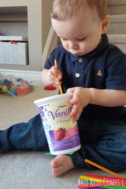 Small toddler putting an orange popsicle stick into a container