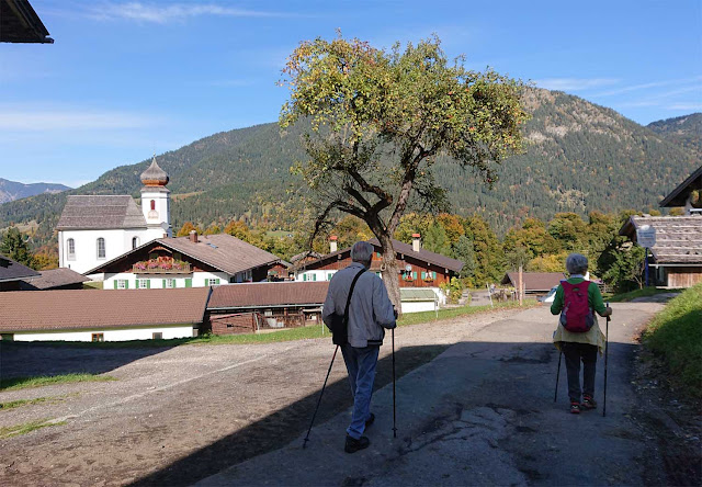 Wanderer mit Stöcken im Kirchdorf Wamberg, St. Anna Kirche im Hintergrund 