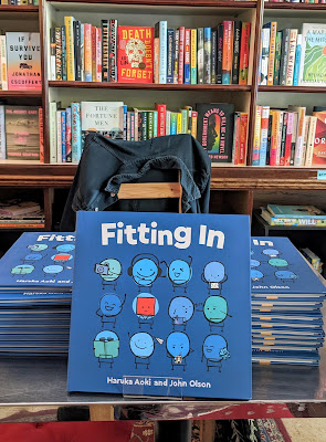 A photo of three stacks of “Fitting In” picture books in front of a book shelf filled with books at a book store