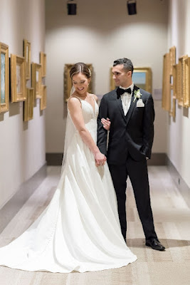 bride and groom holding hands in hallway surrounded by artwork