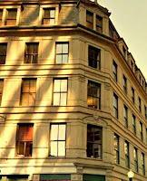 5 story office building, tan exterior with striped reflections from nearby modern office tower