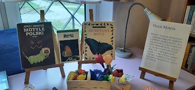 Na sztalugach trzy książki o motylach oraz napis Dzień motyla. Pod sztalugami motyle i kwiaty w wiklinowym koszyku