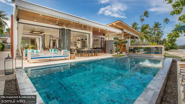 A blue pool with sun loungers in the background and a villa with open bifold doors behind