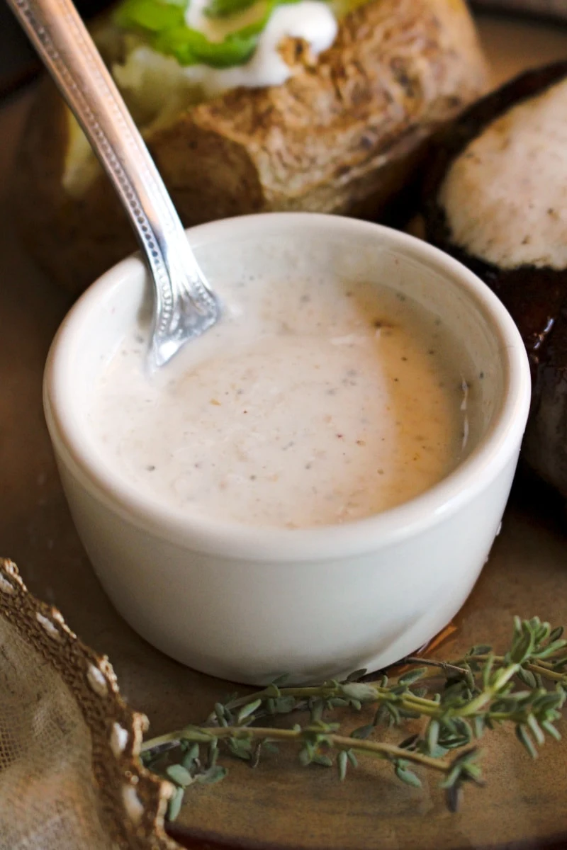 A small white cup of Creamy Horseradish Sauce with a silver spoon in it.