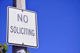 Black and White Sign Saying No Soliciting on Post Against Blue Sky