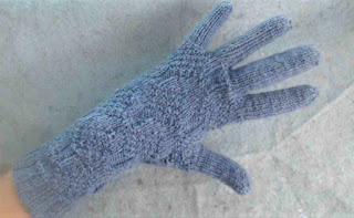 someone wearing a light blue glove, knit in fingering-weight yarn with a knit and purl texture on the cuff and hand