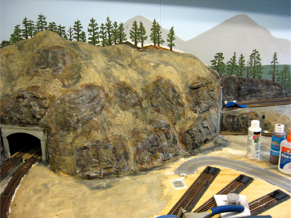 A wash of thinned black acrylic paint being applied to plaster hard shell terrain and plaster rock outcroppings