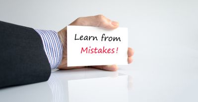 A man's hand holding a card which says, "Learn from mistakes".