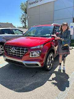 Me standing in front of a red Hyundai Venue, a small SUV with a silver roof rack.