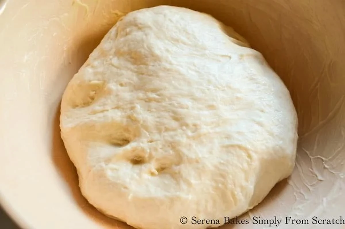 A down shot of Potato Roll dough in a cream colored bowl greased with butter.