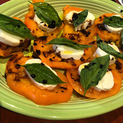 large slices of yellow tomato topped with slices of basil and a single basil leaf, dotted with balsamic vinegar