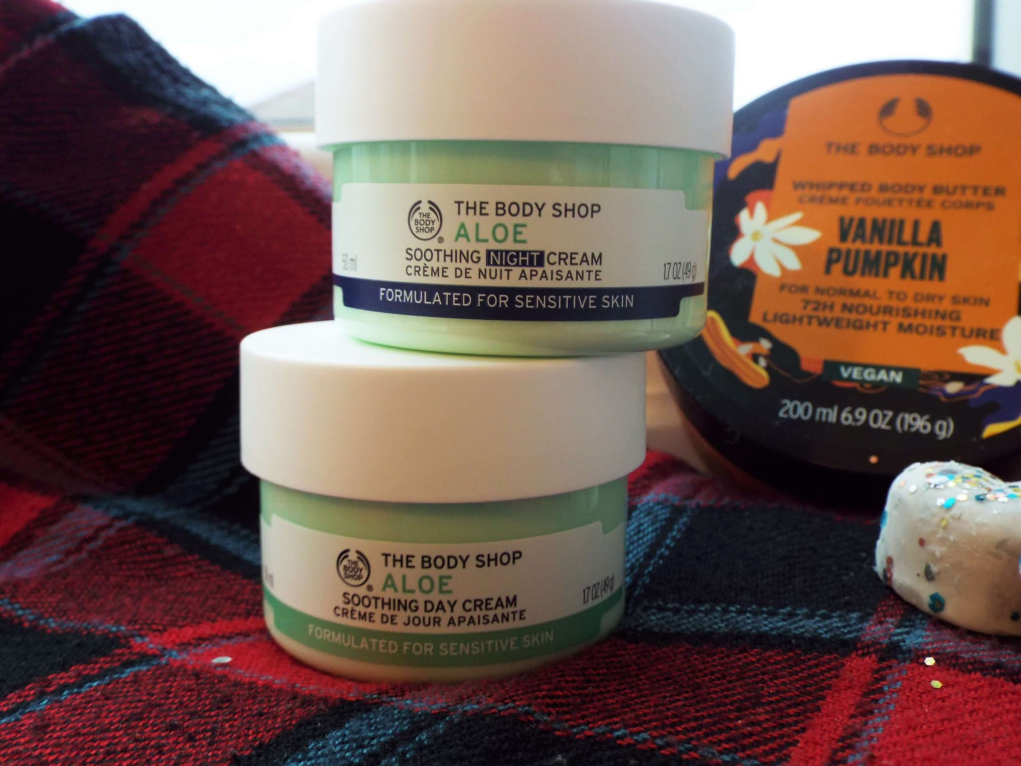 The Body Shop Soothing Aloe Night and Day Cream, sat on top of each other in green tubs, on tartan scarf.