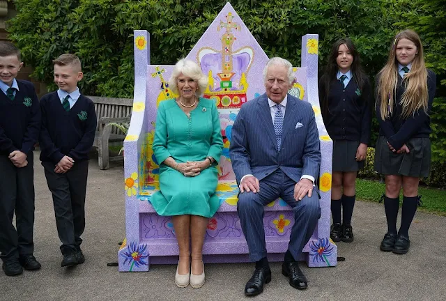 Queen Camilla wore a blue midi dress. The Queen wore an ivory two-tone coat and white midi dress. Coronation Garden in Newtownabbey