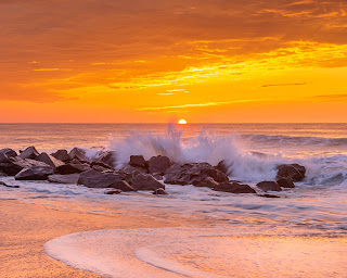 A wide perspective of waves crashing over rocks with the sun peeking over the horizon - Ocean Grove, New Jersey